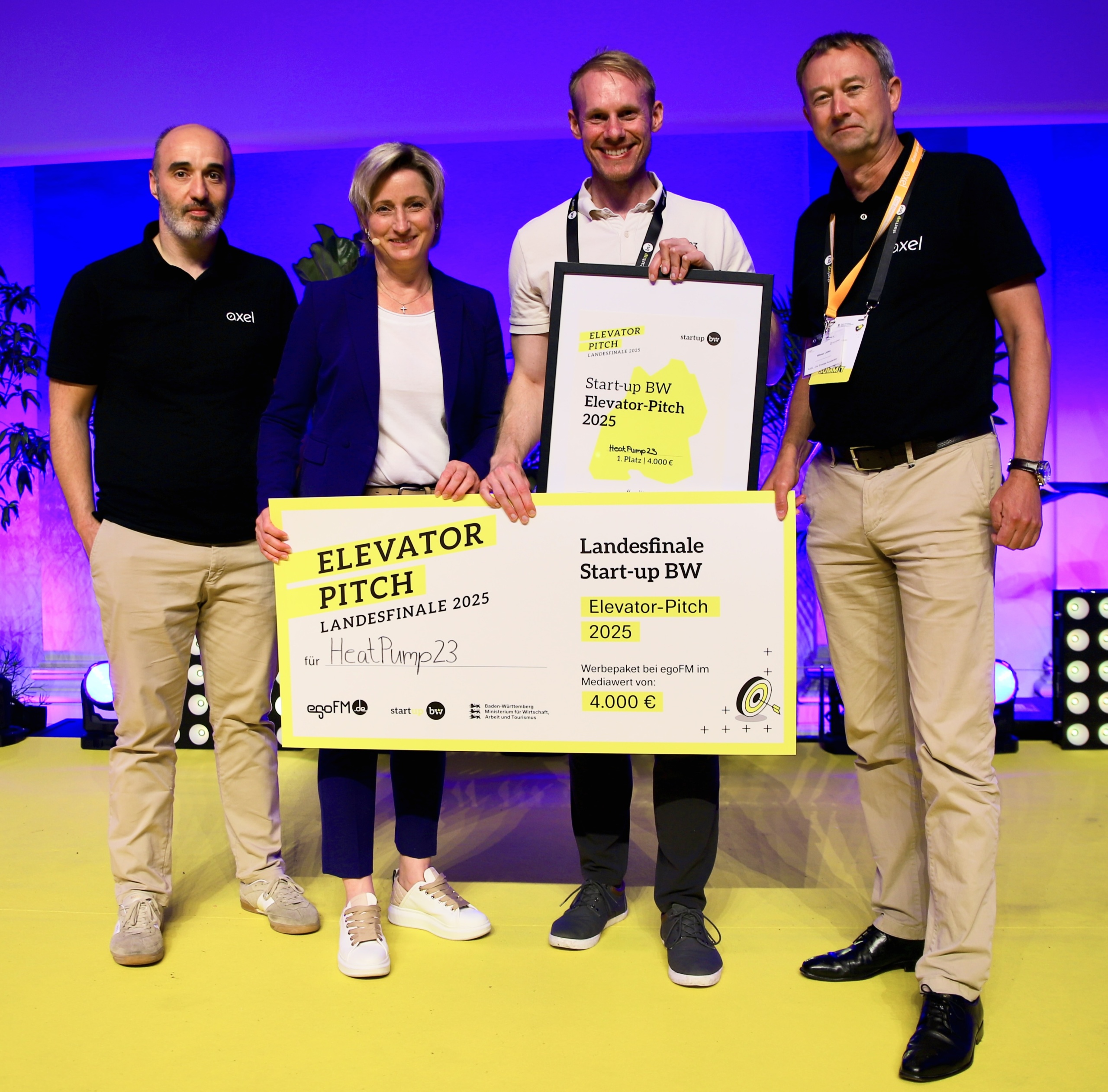 Vier Personen stehen auf einer Bühne, halten ein Schild „Elevator Pitch 2025 für HeatPump23“ und eine Urkunde für den 1. Platz beim Start-up BW Elevator-Pitch.