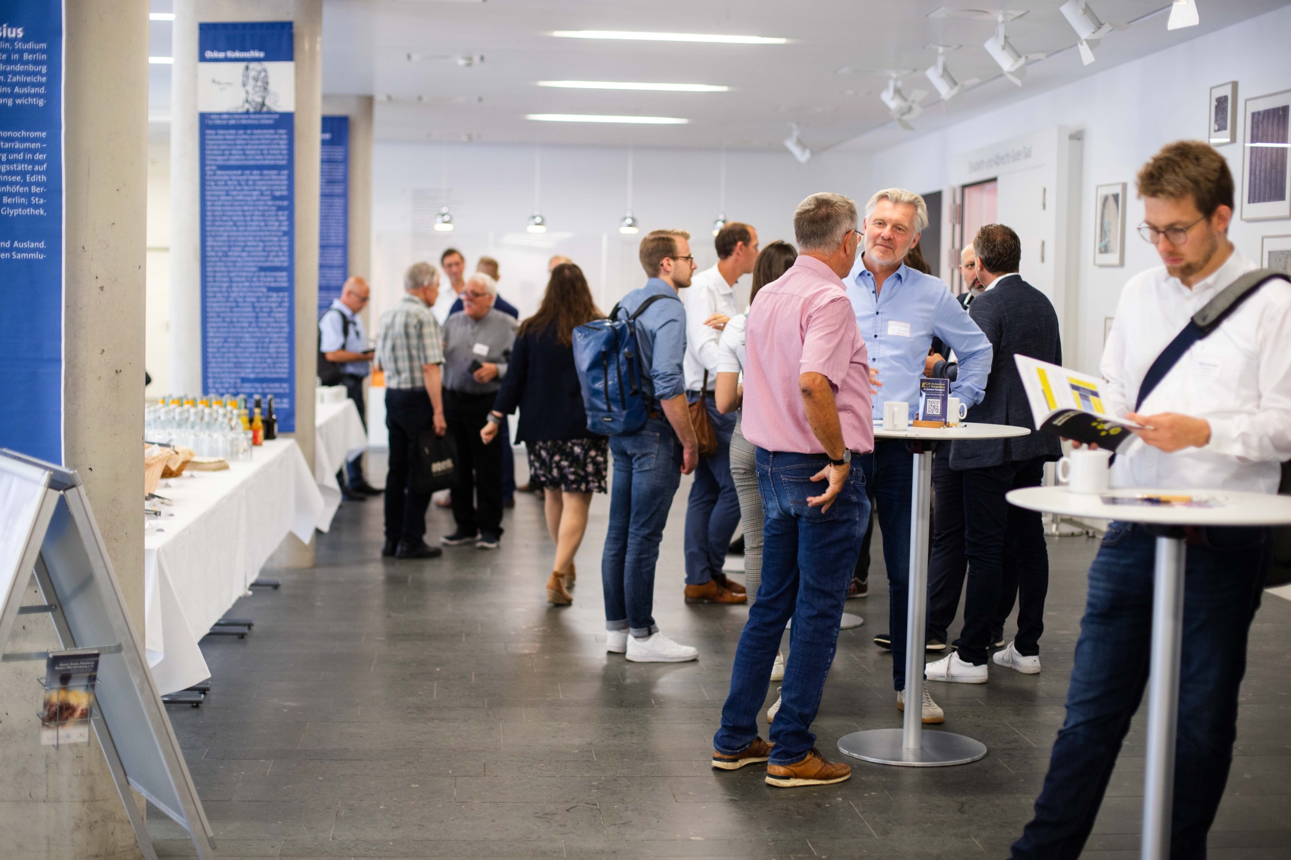 Foto: SmartGridsBW (Lea-Philine Beyer) Smart Grids-Gespräche zum Thema Resilienz: Wie wir kritische Infrastrukturen sichern können. Mehrere Menschen stehen in der Vorhalle an Stehtischen und unterhalten sich bei harmonischer Atmosphäre.
