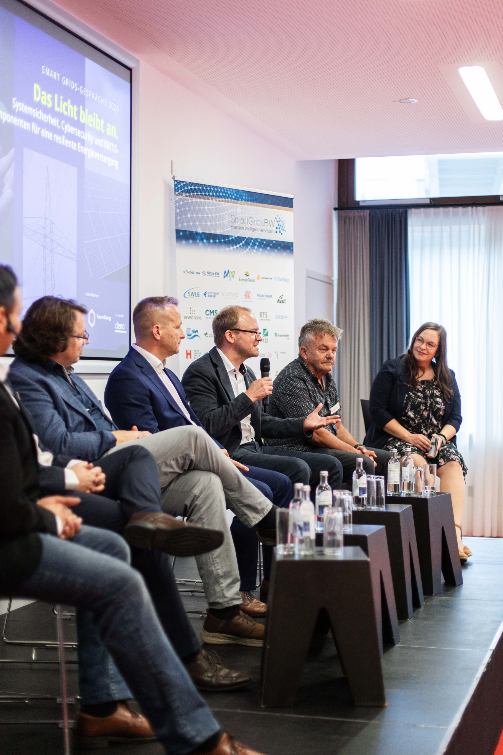 Foto: SmartGridsBW (Lea-Philine Beyer) Smart Grids-Gespräche zum Thema Resilienz: Wie wir kritische Infrastrukturen sichern können. Mehrere Menschen stehen in der Vorhalle an Stehtischen und unterhalten sich bei harmonischer Atmosphäre.