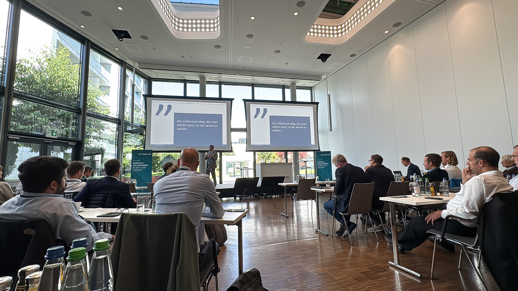 Blick in den Konferenzraum der Veranstaltung „TRANSFORM 2025“ mit Vortrag auf zwei Leinwänden und Teilnehmenden im Publikum.