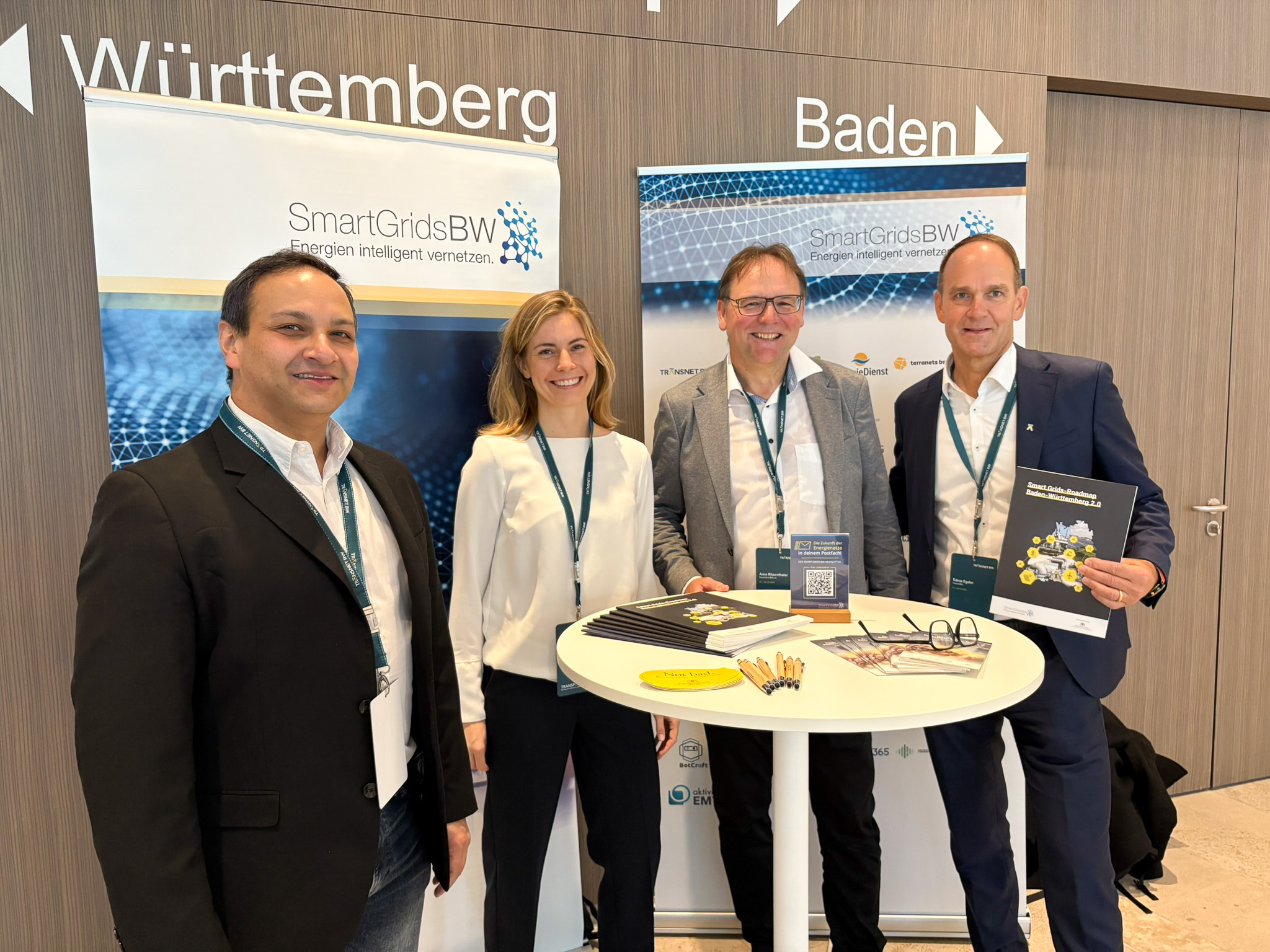 Vier Teilnehmende der SmartGridsBW vor Messestand-Bannern von „Baden-Württemberg“ und „Baden-Württemberg – Smart Grids BW“. (Gruppenfoto am Ausstellungsstand)