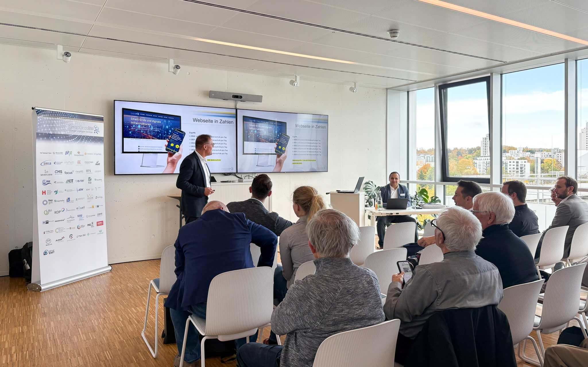 Vortrag während der SmartGridsBW-Gespräche 2025: Ein Referent stellt Kennzahlen zur SmartGridsBW-Webseite vor, während Teilnehmende aufmerksam zuhören.