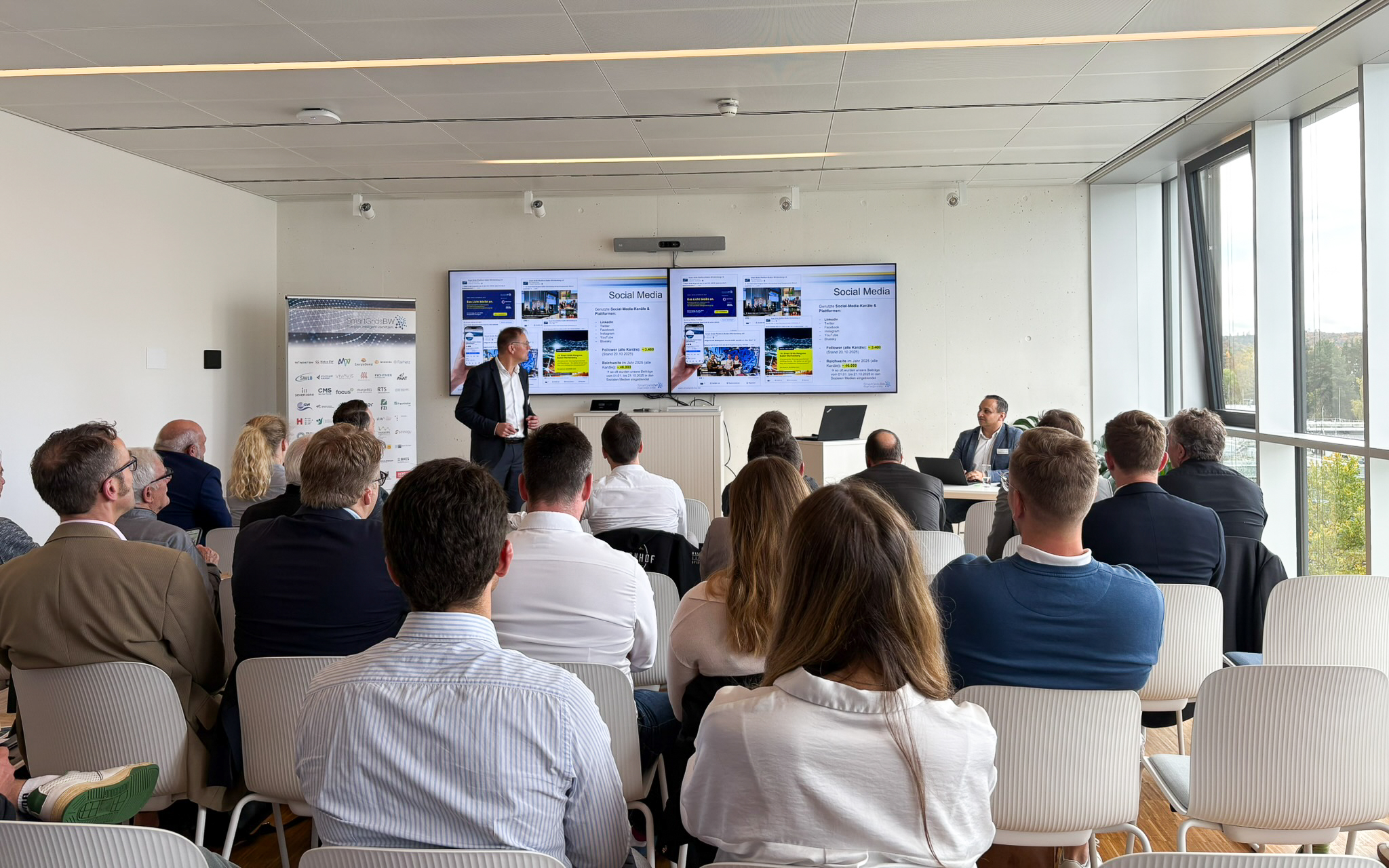 Vortrag während der SmartGridsBW-Gespräche 2025: Ein Referent stellt Kennzahlen zur SmartGridsBW-Webseite vor, während Teilnehmende aufmerksam zuhören.