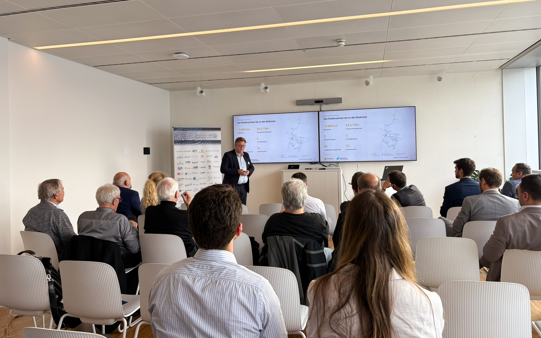 Vortrag während der SmartGridsBW-Gespräche 2025: Ein Referent stellt Kennzahlen zur SmartGridsBW-Webseite vor, während Teilnehmende aufmerksam zuhören.