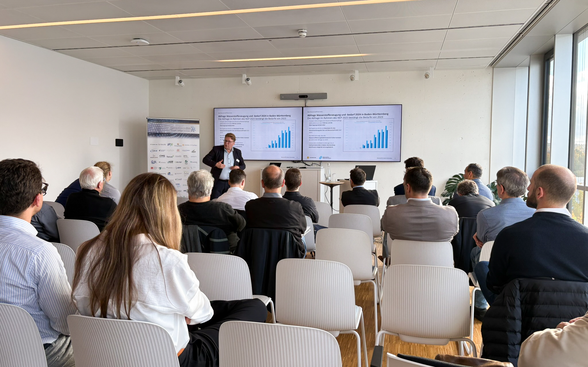 Vortrag während der SmartGridsBW-Gespräche 2025: Ein Referent stellt Kennzahlen zur SmartGridsBW-Webseite vor, während Teilnehmende aufmerksam zuhören.