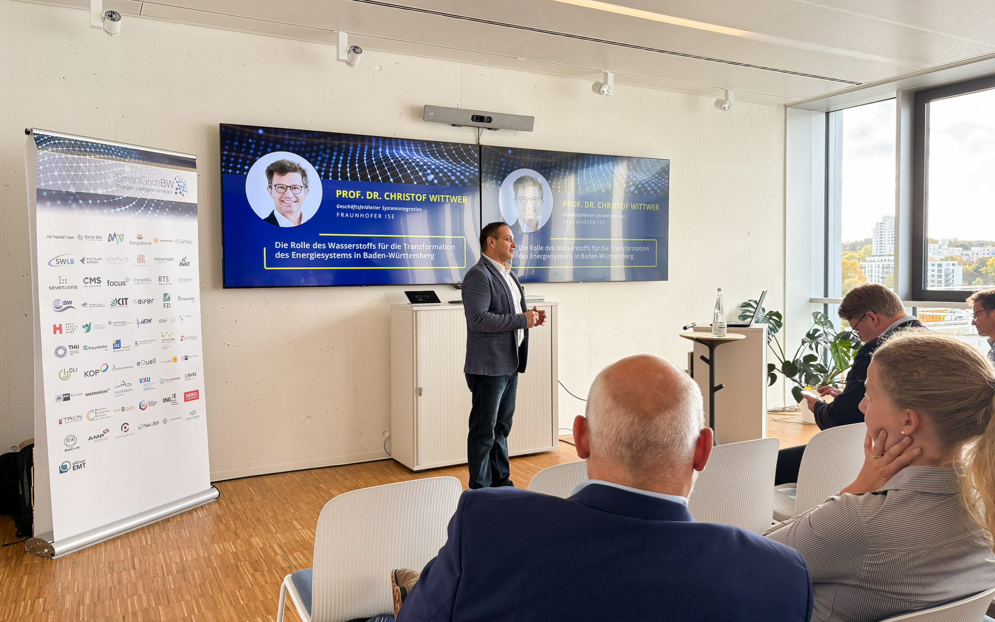 Vortrag während der SmartGridsBW-Gespräche 2025: Ein Referent stellt Kennzahlen zur SmartGridsBW-Webseite vor, während Teilnehmende aufmerksam zuhören.