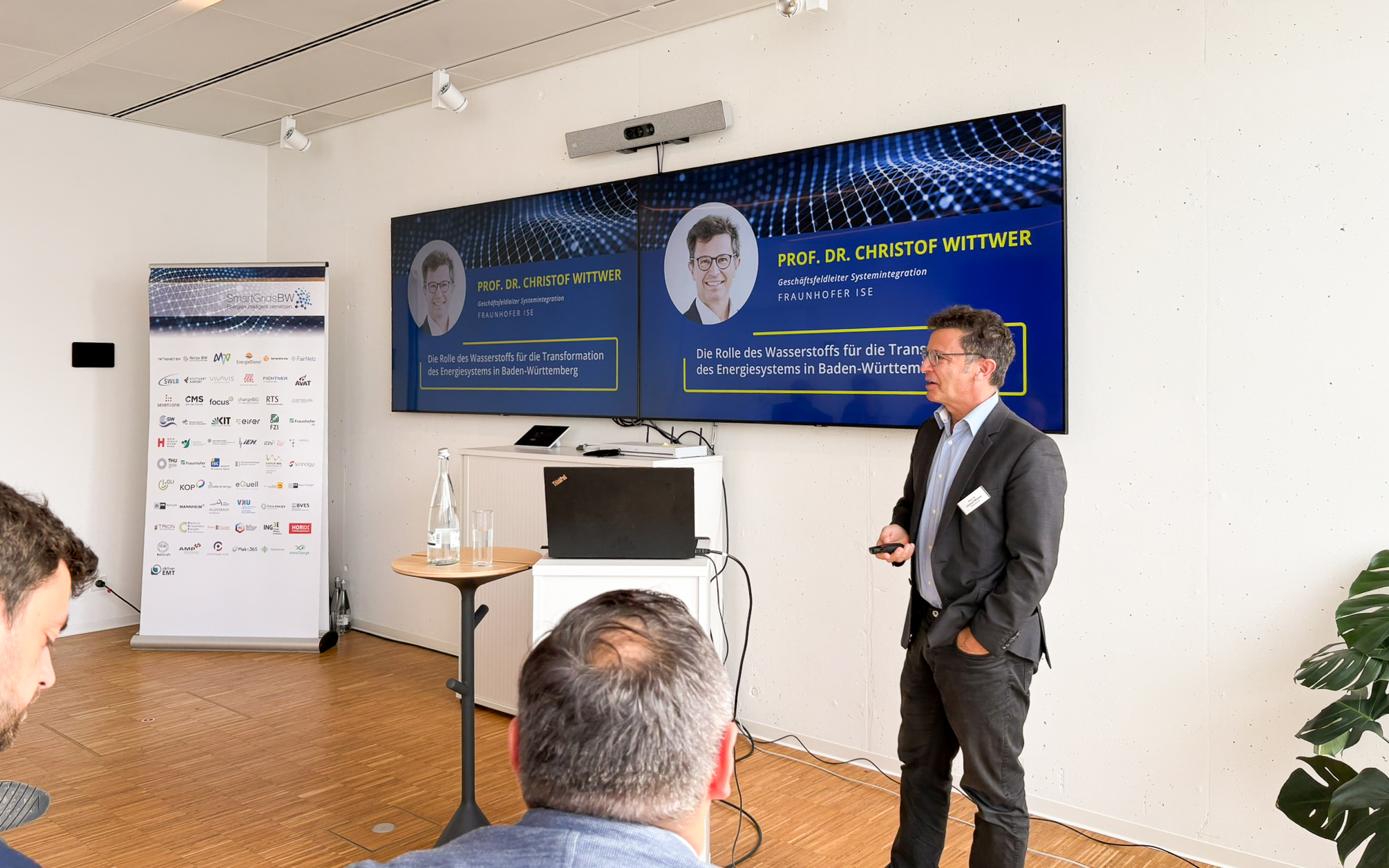 Vortrag während der SmartGridsBW-Gespräche 2025: Ein Referent stellt Kennzahlen zur SmartGridsBW-Webseite vor, während Teilnehmende aufmerksam zuhören.