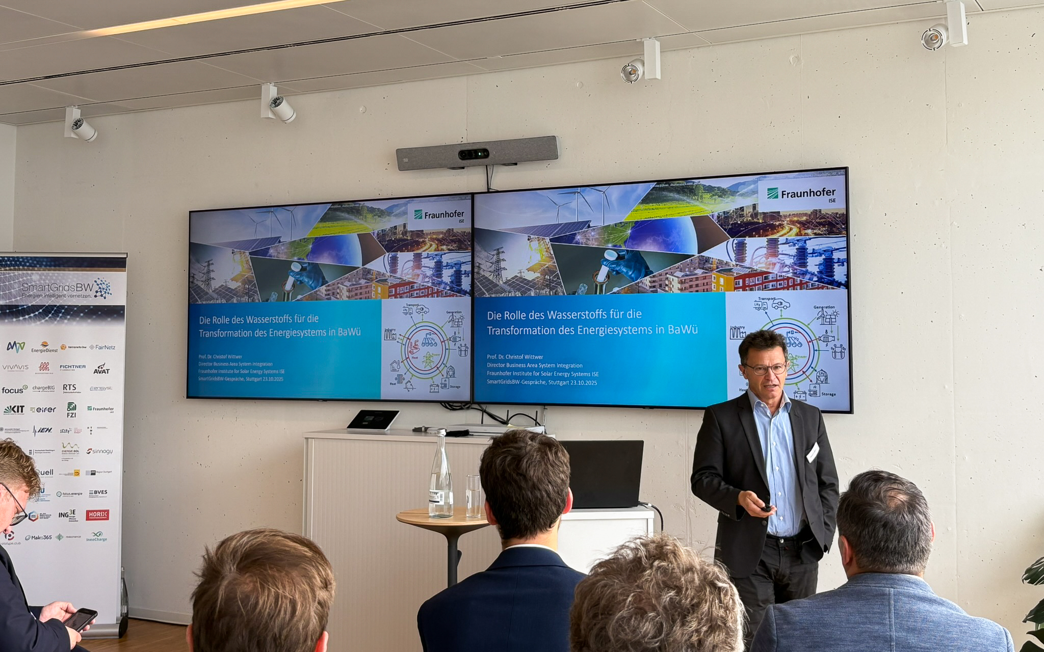 Vortrag während der SmartGridsBW-Gespräche 2025: Ein Referent stellt Kennzahlen zur SmartGridsBW-Webseite vor, während Teilnehmende aufmerksam zuhören.