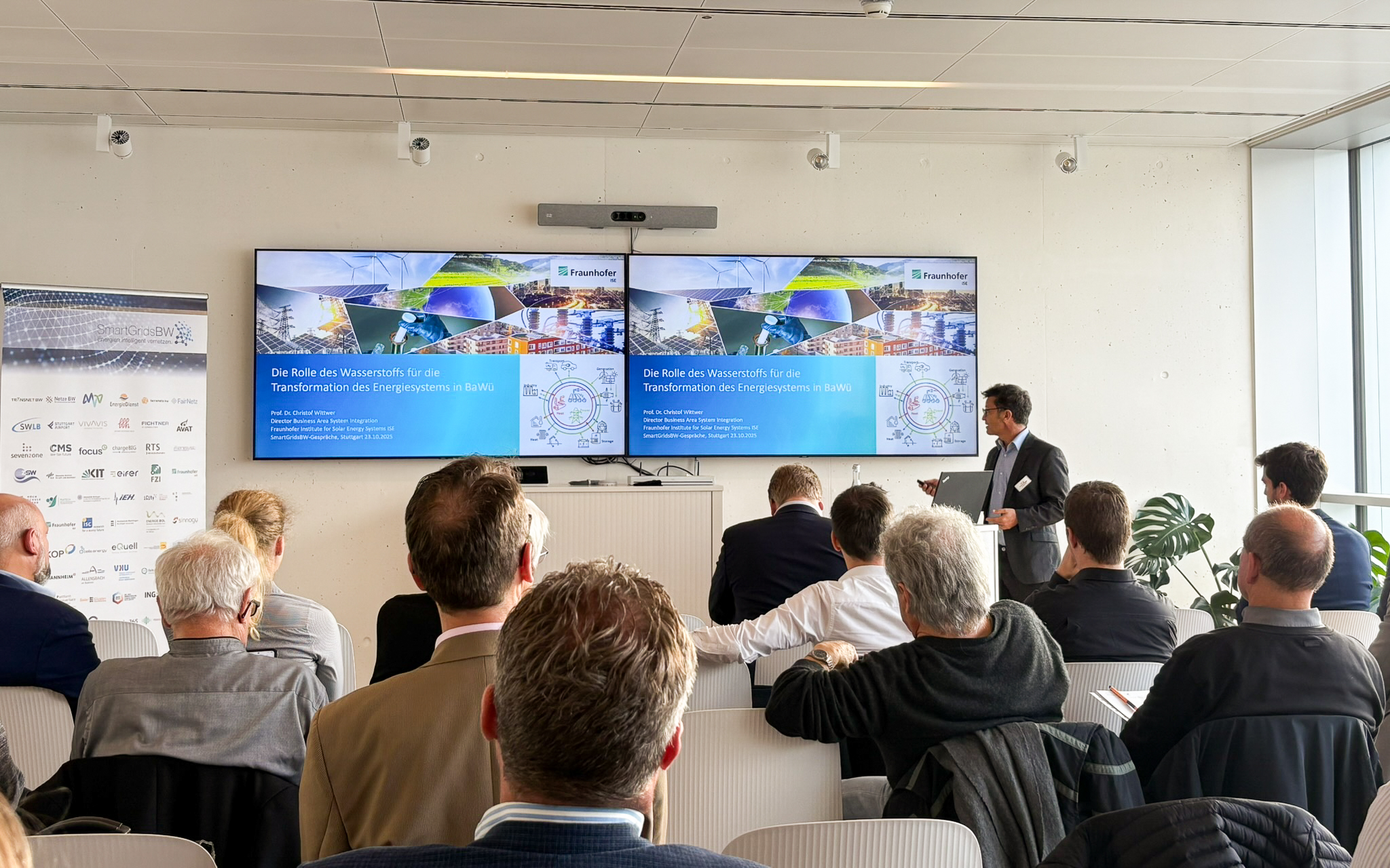 Vortrag während der SmartGridsBW-Gespräche 2025: Ein Referent stellt Kennzahlen zur SmartGridsBW-Webseite vor, während Teilnehmende aufmerksam zuhören.