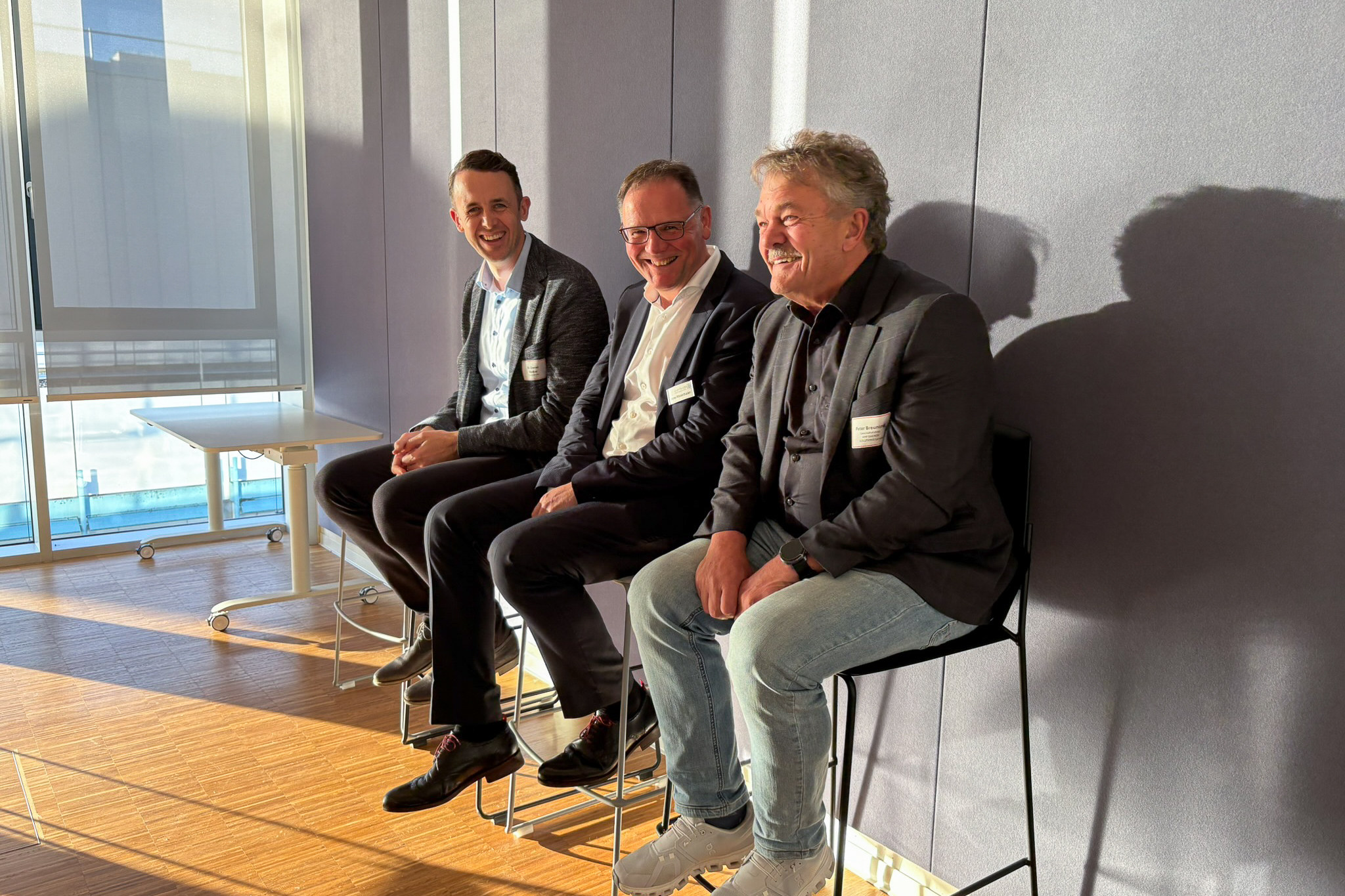 Drei Personen sitzen auf Bistrostühlen und lachen gemeinsam: Der Geschäftsführer und zwei Vorstände von smartGridsBW.
