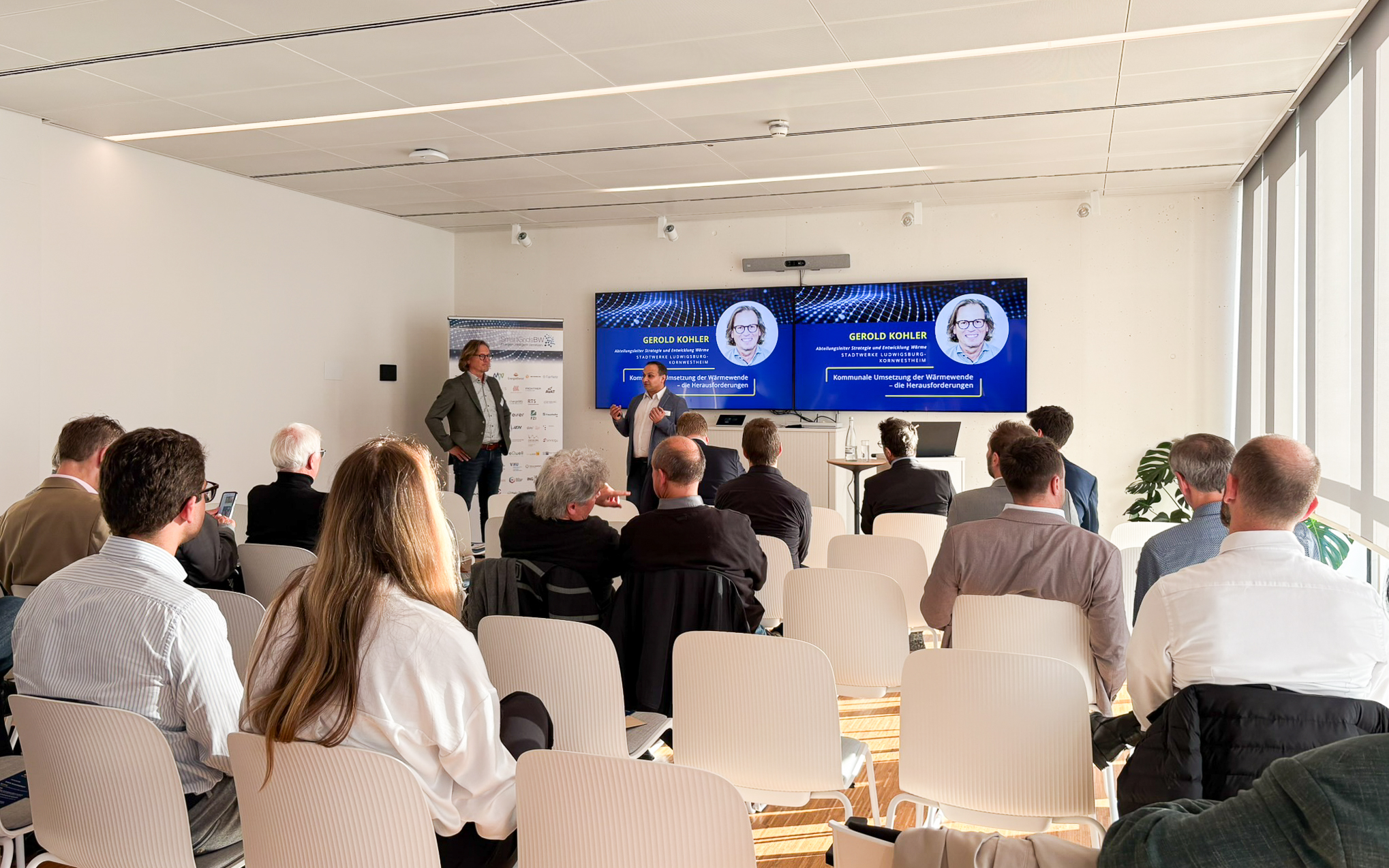 Vortrag während der SmartGridsBW-Gespräche 2025: Ein Referent stellt Kennzahlen zur SmartGridsBW-Webseite vor, während Teilnehmende aufmerksam zuhören.